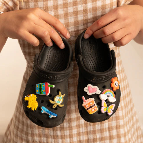 Black clogs with colorful chino charms held by a person wearing a plaid shirt.