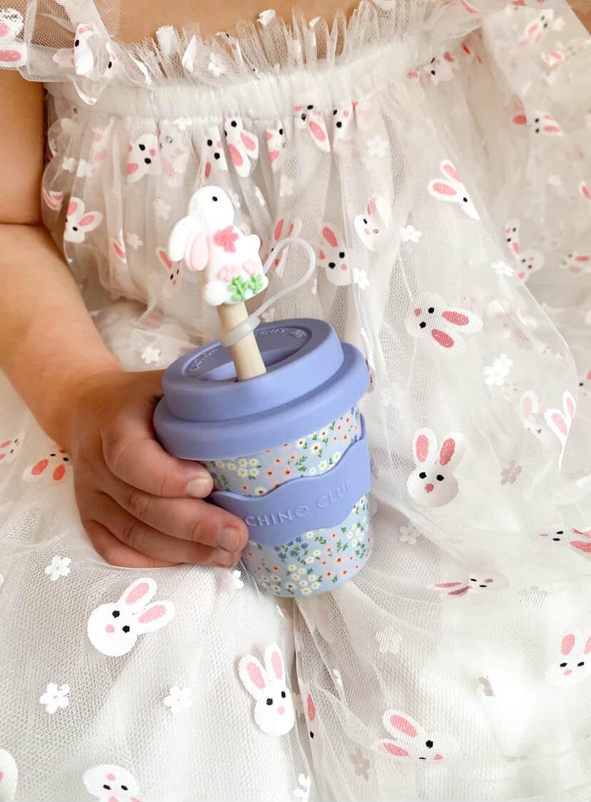 Girl holding a blue floral babychino cup in bunny dress with straw