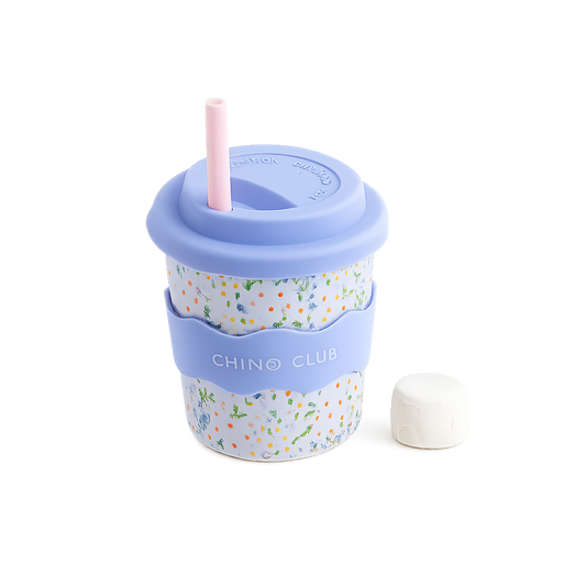 A melamine travel cup with a light blue lid and straw, a floral patterned body, a light blue carrying strap labeled 'CHINO CLUB', and a small white cap placed beside it on a white background.