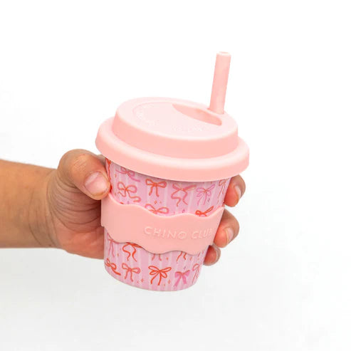Pink babyccino cup 4oz with bow pattern held by a hand on a white background