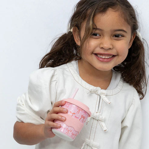Young girl holding a pink cup with a straw against a white background
