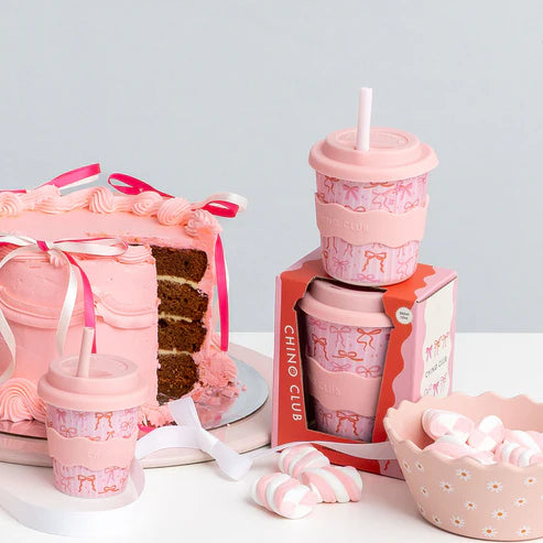 Pink-themed bow babychino cups set including cups, a cake, and a bowl on a light grey background
