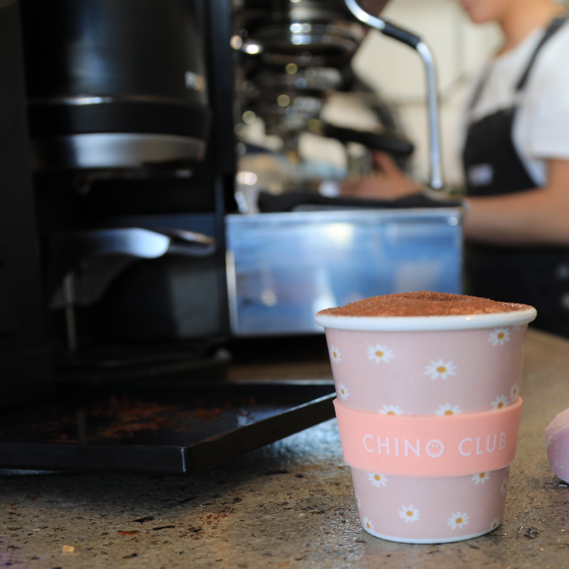 A pink daisy print babychino cup with chocolate powder on the babychino