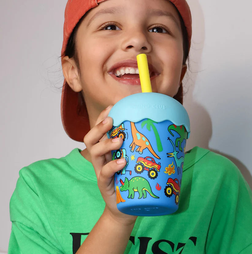 Child drinking from a blue tumbler with colorful designs against a plain background