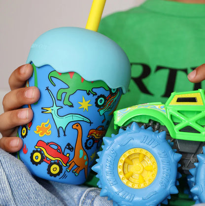 Child holding a colorful dinosaur-themed tumbler with a toy truck in the background