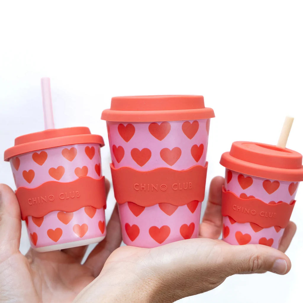 Three Chino Club cups with heart patterns held in a hand against a white background