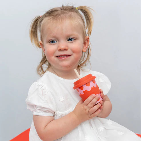 girl holding babychino cup with lid and straw in heart print