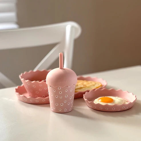 Pink silicone breakfast set with a cup, plate, and bowl on a white surface.