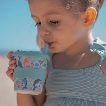 Young girl holding a light blue cup with sea animal design against a clear sky.