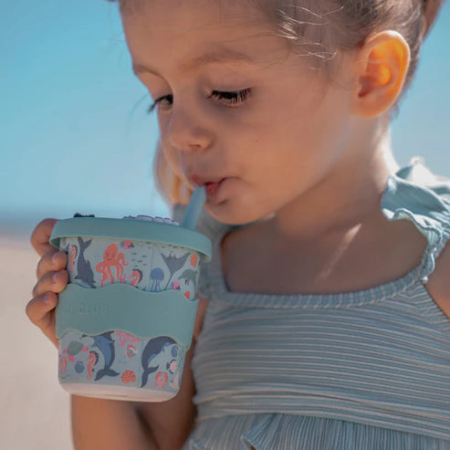 Young girl holding a light blue cup with sea animal design against a clear sky.
