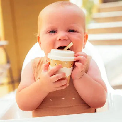 baby holding yellow babychino cup with straw